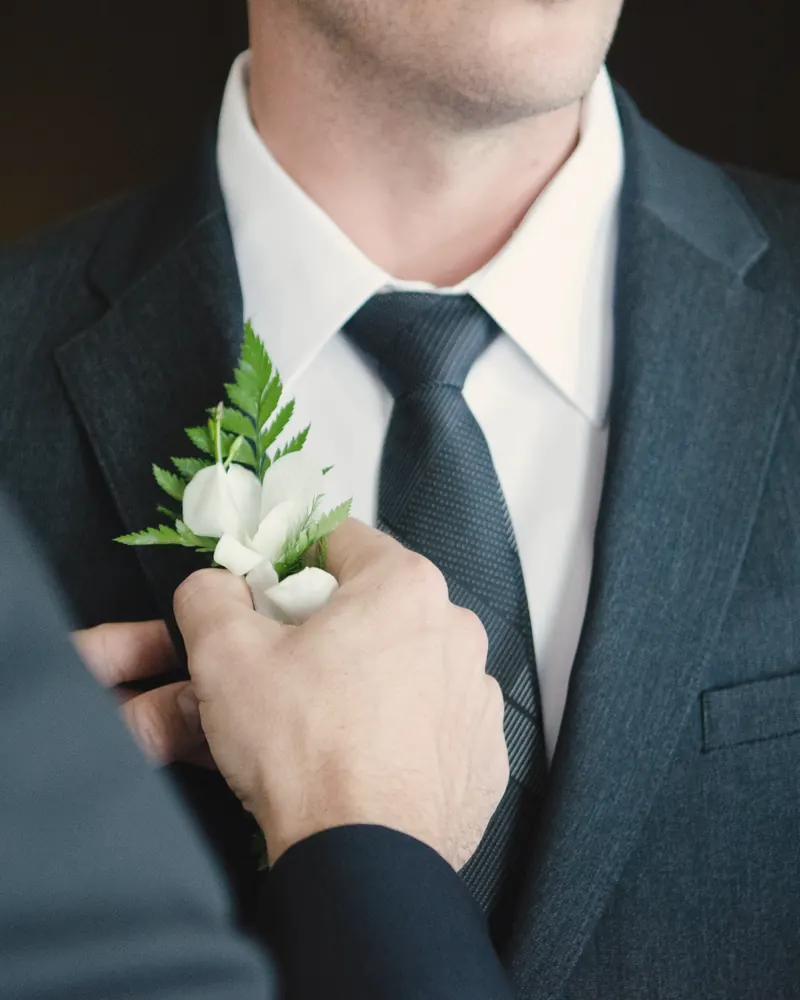 Novio con traje oscuro colocándose el prendido de flores en la solapa