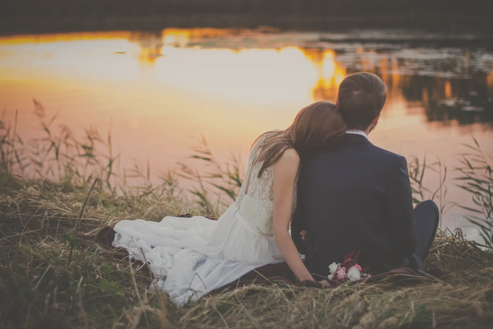 Una pareja de novios sentada junto a un lago al atardecer
